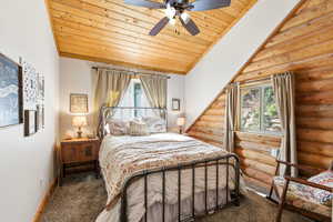 Carpeted bedroom featuring a vaulted wooden ceiling, multiple windows, ceiling fan, and log walls