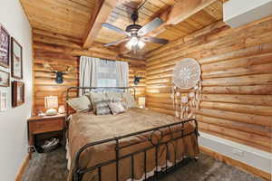 Bedroom with rustic walls, a ceiling fan, a wooden ceiling with exposed beams, and carpet