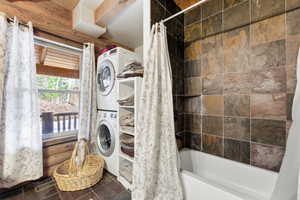 Bathroom featuring stacked washer / dryer, shower / bath combination with curtain, and dark tile patterned floors