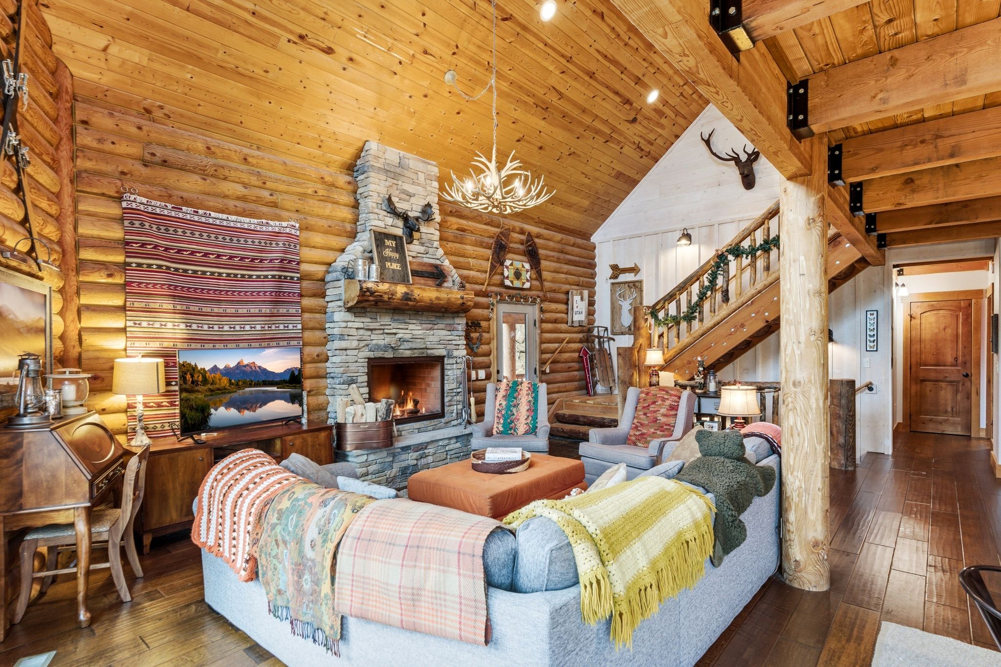 Living room with hardwood / wood-style floors, a chandelier, a stone fireplace, log walls, and a high wood beamed ceiling