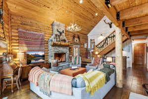 Living room with hardwood / wood-style floors, a chandelier, a stone fireplace, log walls, and a high wood beamed ceiling