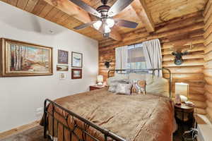 Carpeted bedroom with rustic walls, a ceiling fan, and a wood ceiling with exposed beams