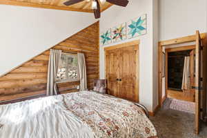 Bedroom featuring log walls, dark carpet, a closet, a ceiling fan, and a vaulted wood ceiling