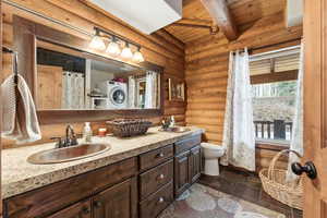 Bathroom featuring rustic walls, double vanity, stone tile floors, a wooden ceiling with exposed beams, and a shower with shower curtain