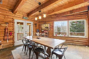 Dining space with rustic walls, wood-type flooring, french doors, healthy amount of natural light, and a wooden ceiling with exposed beams