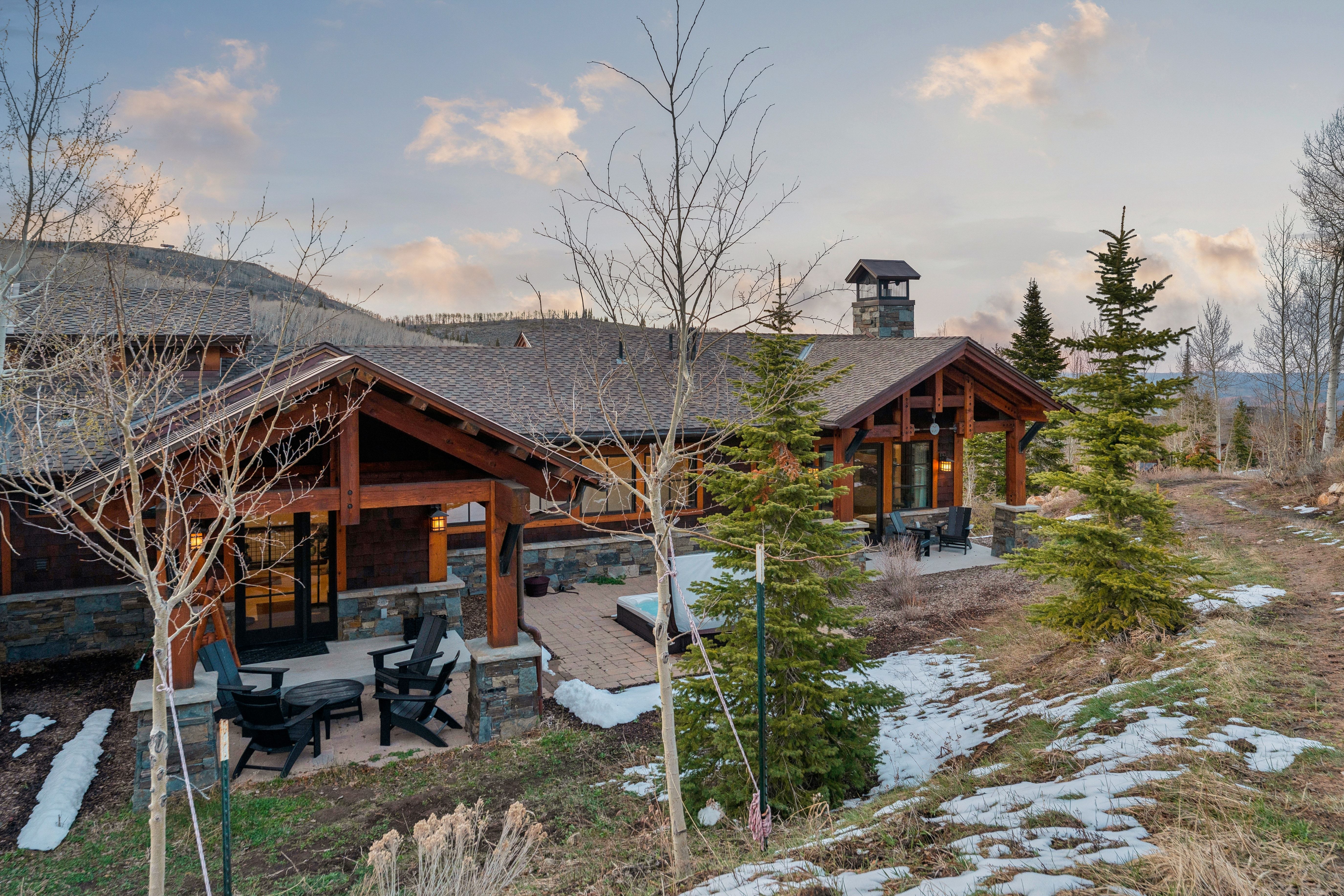 Back of property at dusk featuring a patio area, stone siding, a chimney, and roof with shingles