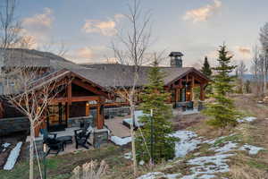 Back of property at dusk featuring a patio area, stone siding, a chimney, and roof with shingles