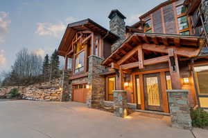 Entrance to property featuring an attached garage, stone siding, driveway, and a chimney