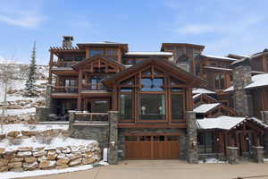 View of front facade with concrete driveway, a garage, a chimney, stone siding, and a balcony