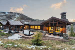 Back of property at dusk featuring a patio area, a chimney, solar panels, and stone siding