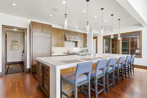 Kitchen featuring light stone counters, a large island, a kitchen bar, built in fridge, and hanging light fixtures