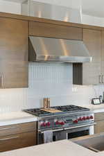 Kitchen with ventilation hood, double oven range, modern cabinets, wood finish cabinetry, and decorative backsplash
