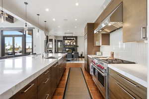 Kitchen with modern cabinets, double oven range, dark wood-style flooring, and light stone countertops