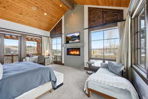 Bedroom with carpet floors, a glass covered fireplace, a high wood beamed ceiling, and recessed lighting