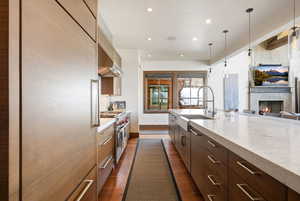 Kitchen with a large fireplace, modern cabinets, light stone countertops, designer range, and range hood