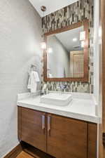 Bathroom with vanity, decorative backsplash, wood finished floors, and wallpapered walls