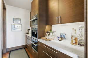 Kitchen with modern cabinets, dark wood-type flooring, light stone countertops, and dark wood finish cabinets