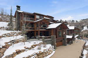 View of front of home with a chimney, an attached garage, concrete driveway, and stone siding