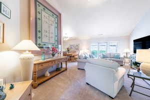 Living area with lofted ceiling, a ceiling fan, and light carpet