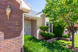 View of exterior entry with stucco siding, roof with shingles, and a yard