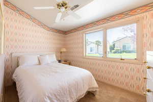 Carpeted bedroom with wallpapered walls and ceiling fan