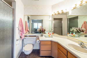 Bathroom featuring wallpapered walls, vanity, a shower stall, a textured ceiling, and dark tile patterned flooring