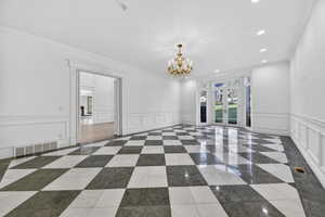 Dining room featuring chandelier and recessed lighting, a decorative wall, ornamental molding, marble and inlaid floor details, and wainscoting