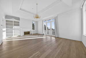Primary suite with chandelier, a tray ceiling, hardwood flooring, ornamental molding, and a fireplace