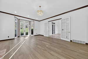 Study featuring french doors, crown molding, hardwood flooring, and chandelier