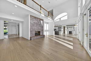 Unfurnished living room featuring a brick fireplace, ornamental molding, hardwood flooring, a high ceiling, and recessed lighting