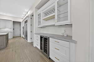 Indoor dry bar featuring hardwood flooring, glass insert cabinets, stone counters, dual tone cabinetry, and wine cooler