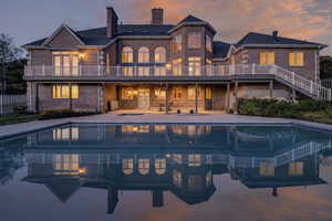 Back of property at dusk with a chimney, brick siding, an outdoor pool, and a balcony