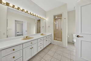 Bathroom with double vanity, a shower stall, and light tile floors