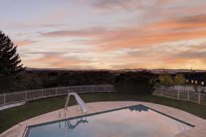 Pool at dusk with a fenced backyard, a patio, and a water slide