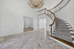 Entryway with hanging lights, a decorative wall, marble flooring, wainscoting, and a high ceiling