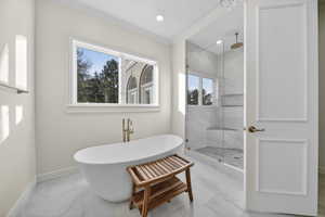 Primary suite bathroom featuring light marble finish flooring, a marble finish shower, a freestanding bath, crown molding, and recessed lighting