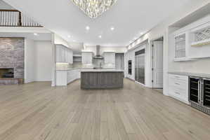 Kitchen featuring a kitchen island with sink, a brick fireplace, open shelves, glass fronted cabinets, and stone backsplash