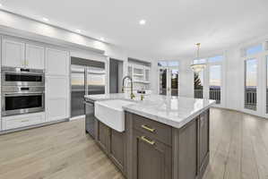 Kitchen with two tone cabinets, a center island with sink, stone counters, Wolf and Sub-Zero stainless steel appliances, and hardwood flooring