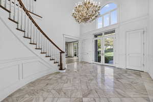 Entryway featuring a decorative wall, a chandelier, french doors, a high ceiling, and marble flooring