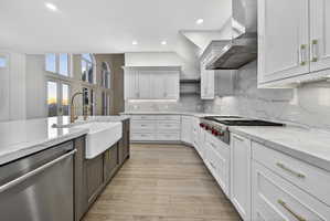 Two tone kitchen featuring stone counters, Wolf stainless steel appliances, two tone cabinetry, hardwood floors, and stone backsplash