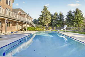 View of swimming pool featuring patio surround, a water slide, and a balcony