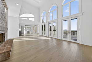 Unfurnished living room featuring a brick fireplace, hardwood flooring, french doors, recessed lighting, and a high ceiling
