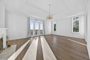Primary suite featuring hardwood floors, a chandelier, a high end fireplace, ornamental molding, and a tray ceiling
