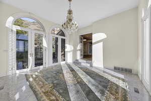 Solarium featuring french doors, marble flooring, and chandelier