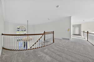 Corridor featuring an upstairs landing, light colored carpet, crown molding, and chandelier