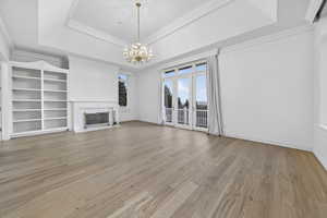Primary suite with a fireplace, chandelier, crown molding, hardwood flooring, and a tray ceiling