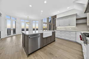 Kitchen featuring two tone cabinetry, stone countertops, Wolf stainless steel appliances, stone backsplash, and hardwood flooring