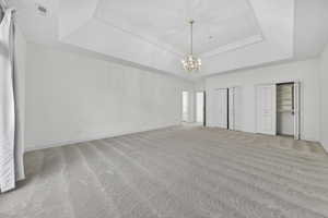 Bedroom featuring two closets, chandelier, light colored carpet, and a tray ceiling