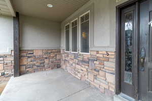 Property entrance with a porch, stone siding, and stucco siding