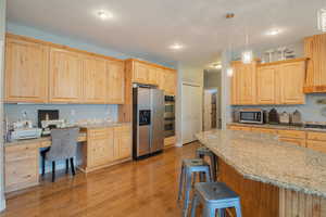 Kitchen with light wood finish cabinets, light stone counters, stainless steel appliances, and light wood-style flooring